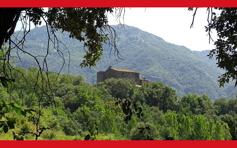 Imatge de la Masia Sala, vista al fons al cim de una muntanya plena de vegetació.