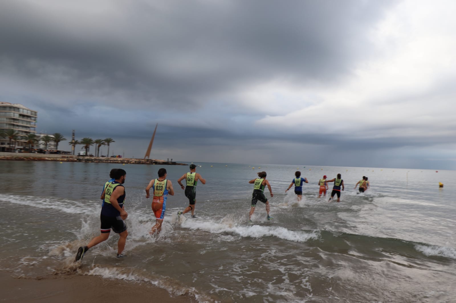 Foto del campionat de marxa aquàtica. En el plànol es veu la platja en persepectiva diagonal i els participants fent marxa per l'aigua.