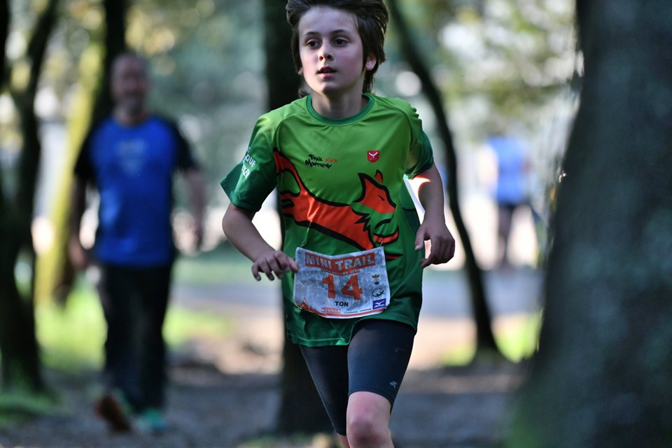 Imatge d'un nen corrents la mini trail, amb el dorsal 14 i una samarreta verda, al bosc