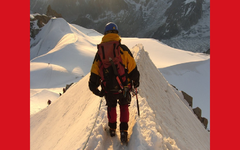 un alpinista d'esquenes al cim d'una muntanya nevada