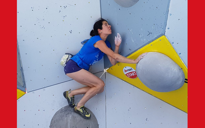 una noia pegada a la pared del roco a punt de fer el següent pas en la pared, fent bloc